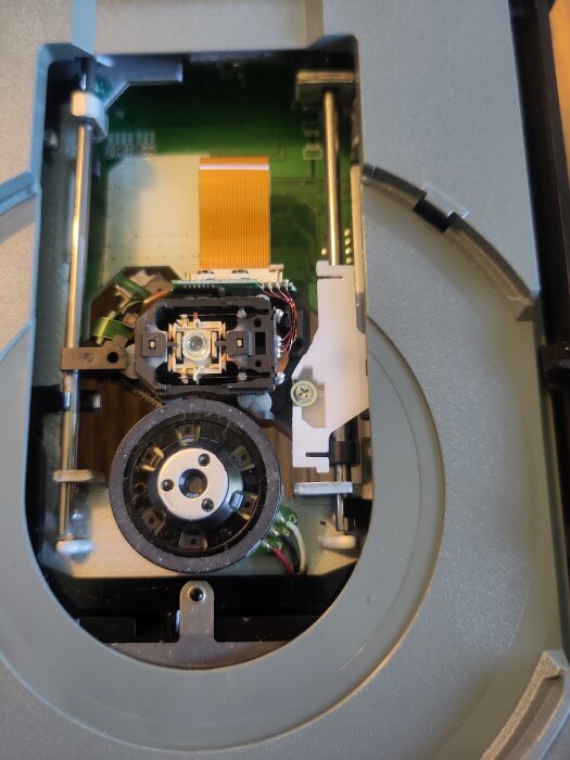 Xbox 360-skivläsare med öppnat hölje, exponerar dess laser- och mekaniska delar. En vit del sitter löst, vilket orsakat läsproblem.