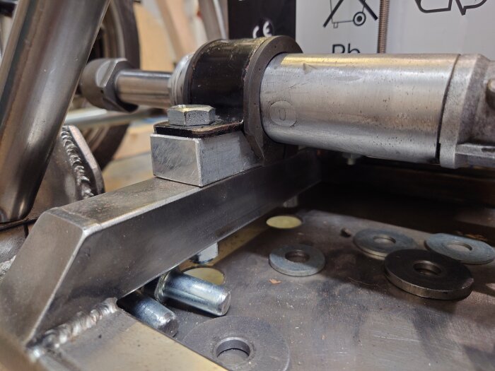 En närbild av en styrväxel med metalldelar och skruvar monterade, med brickor i bakgrunden på en metallplatta.