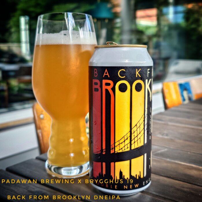 Glas och burk med "Back from Brooklyn" DNEIPA av Padawan Brewing och Brygghus 19, står på ett bord.