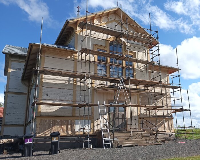 Byggnad med byggnadsställningar för renovering av yttervägg, klarblå himmel i bakgrunden.