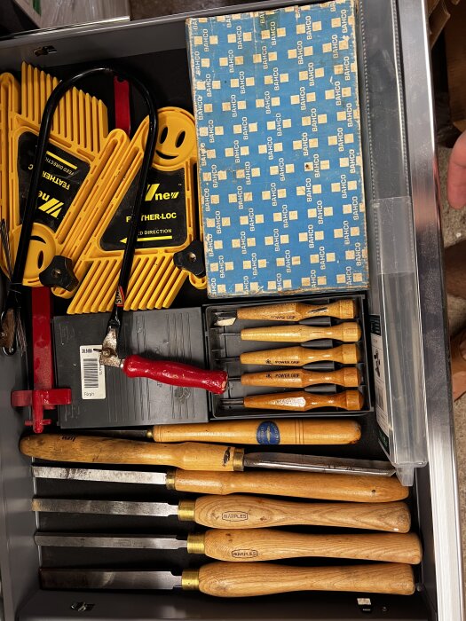 En låda fylld med olika snickeriverktyg, inklusive stämjärn, betvingar och ett paket med Bacho sågblad.