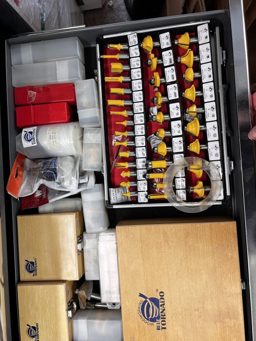 En låda med sorterade fräsbits i ett etui samt flera förvaringslådor i plast och trä med logotypen "Blue Tornado".