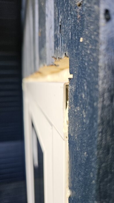 Närbild på en fönsterkant med synliga glipor mellan fönster och ytterpanel, omgiven av blåmålad träpanel och ljus tätningsmassa.