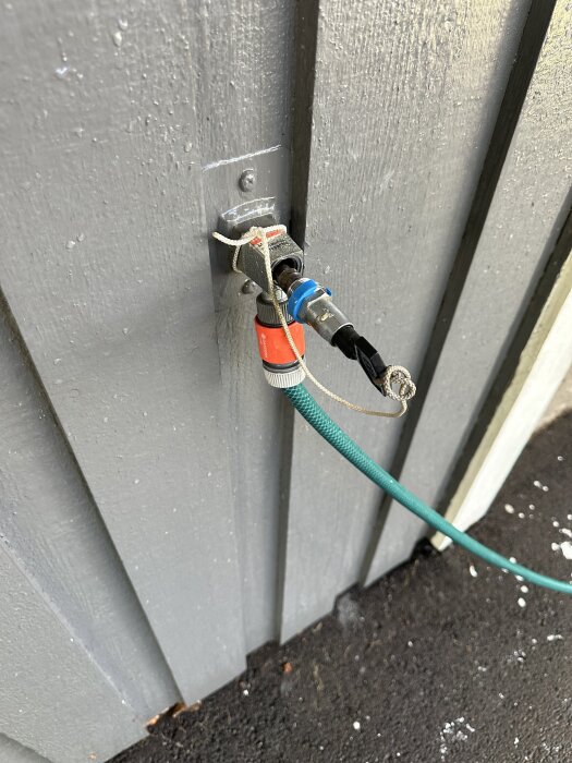 Frostsäkert vattenutkast monterat på en grå trävägg med ansluten grön trädgårdsslang.