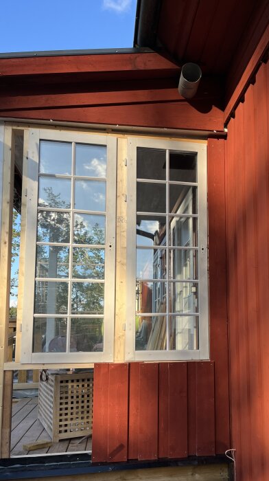 Röd träfasad med vita fönster, byggprojekt utomhus i kvällsljus.