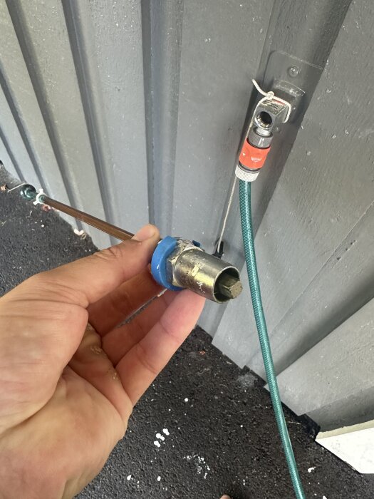 Hand håller lossnat frostsäkert vattenutkast utomhus, fastsatt slang syns.