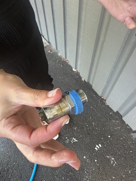 Person håller en frostsäker vattenutkastare med blå packning, framför en grå vägg, på mörk mark.