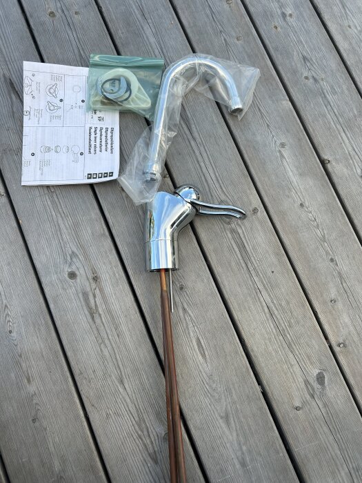 Blandare med kopparrör, gummipackningar i plastpåse och installationsmanual på en trätrall.