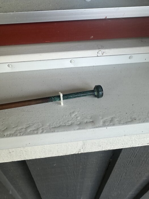 Munstycke monterat på plasthuvud under en röd och vit yta, delvis täckt med färgskav, synlig i byggprojekt.