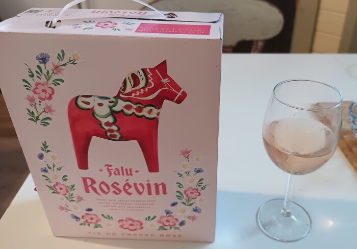 Kartong med Falu Rosévin och ett glas rosévin på ett bord.