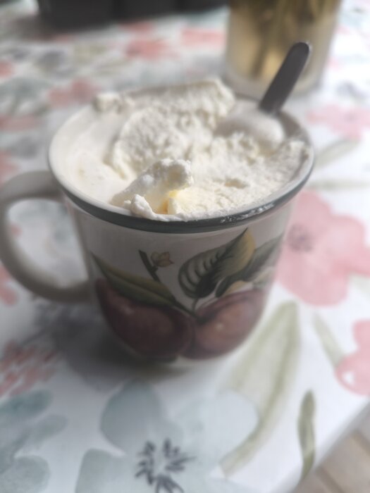Mugg med Irish Coffee, toppad med vispad grädde, placerad på ett bord med blommigt mönster.