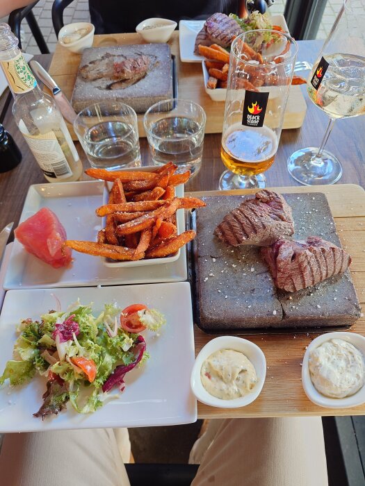 Mixed grill-tallrik på restaurang med oxfilé och tonfisk på het sten, sötpotatispommes, sallad, två såser, samt drycker bredvid.