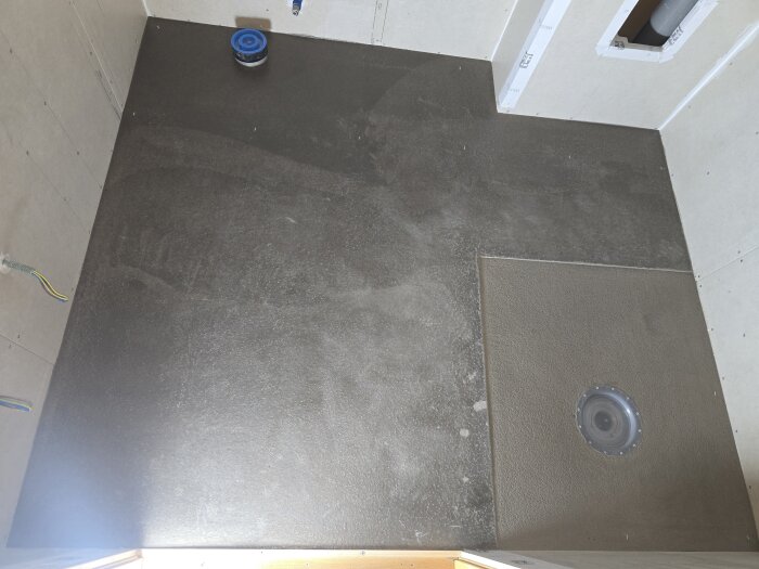 Flytspacklat golv i ett badrum med synlig brunnsfläns och elslingor inspekterade, redo för vidare bearbetning av duschzonen.