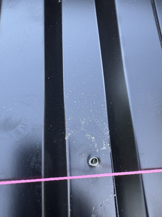 Svart plåt med ofärdig farmarskruv och rosa snöre.