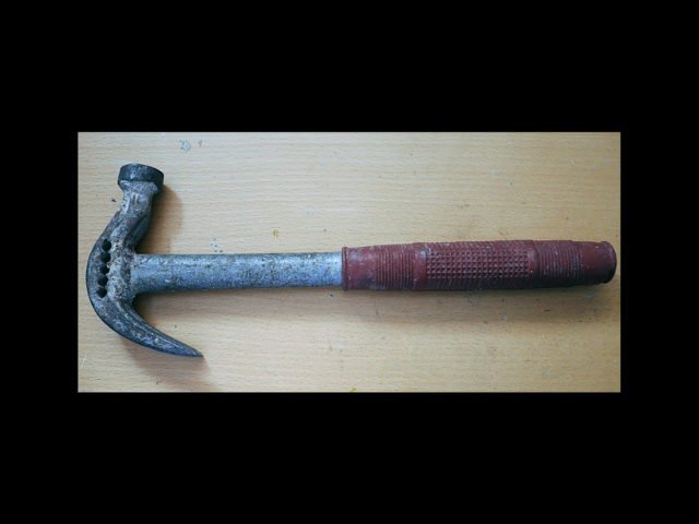 Hammare med rött handtag ligger på träbord.