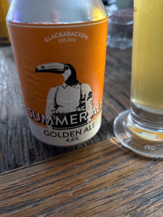 En burk Klackabacken summer ale och ett glas öl på ett träbord.