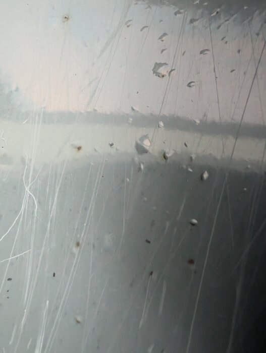 Närbild av glasfiberytan på en badtunna, med små bubblor och bruna fläckar synliga i materialet.