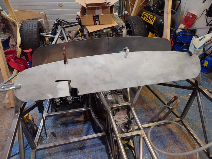 Byggsats av bilram med två metallpaneler monterade, verktyg och kartonger syns i bakgrunden.