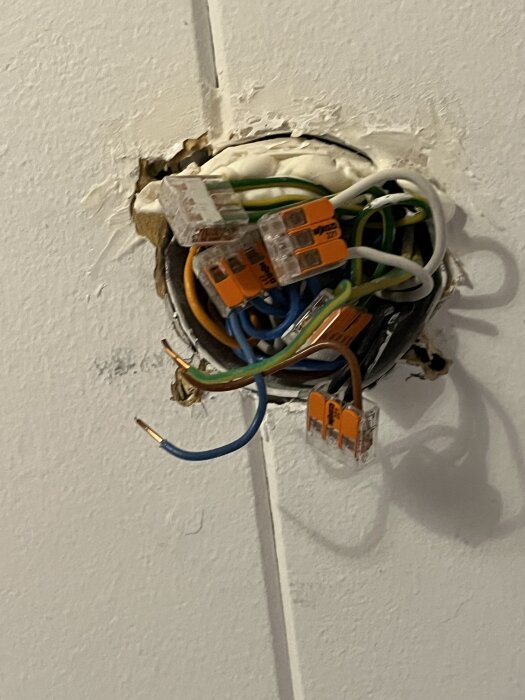 Löst hängande elektriska kablar med kopplingsklämmor i taket på ett radhus byggt 1976, exponerade genom ett trasigt lager gips.