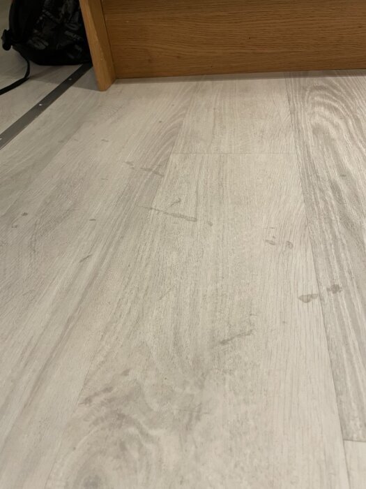 Ljusa trägolv med synliga små mörka fläckar och tecken på erosion nära en tröskel.