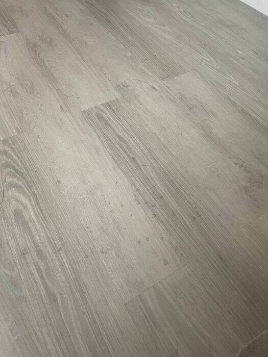 Laminatgolv med små, mörka fläckar och synlig erosion i ytan, visar tecken på nedbrytning och missfärgning efter kort användning.