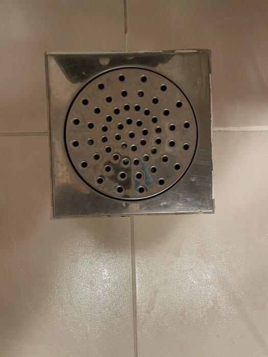 Golvsil i dusch med synlig våtrumsmatta, klämring och vattenlås; krombrunn inte centrerad över den nedre delen.