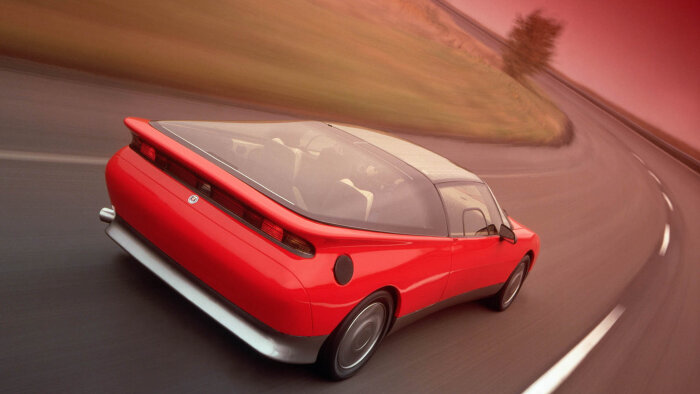 Röd Saab konceptbil från 1985, sedd bakifrån, kör på en landsväg i solnedgång.