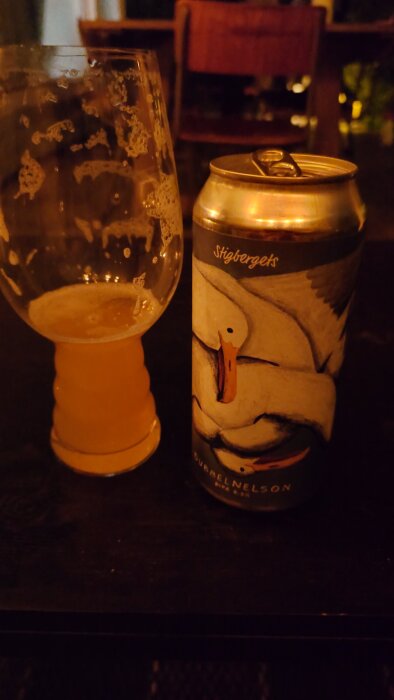 Ölglas och burk med stiliserade fåglar, delvis fylld med gyllengul öl, på ett bord.