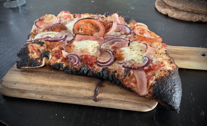 Hemlagad pizza med lök, skinka, ost och tomat på en något bränd kant.