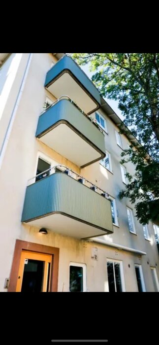 Lägenhetsbalkonger i ett flervåningshus med blå paneler, sedd från markplan.