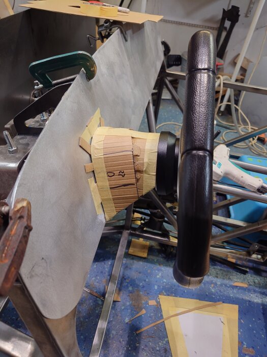 Bilbygge med ratt och pappmall monterad på metallkonstruktion i garage.