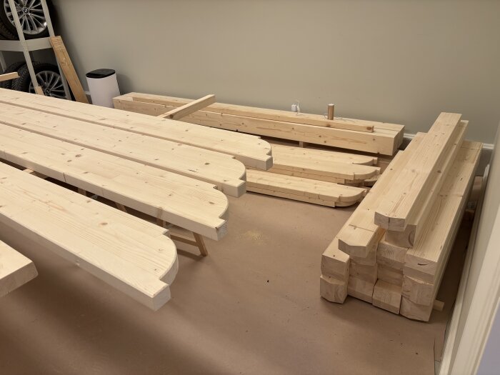 Obehandlade träbalkar och stolpar på golvet, redo för målning, troligen för byggprojekt av en pergola enligt texten i inlägget.