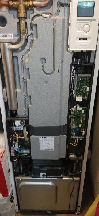 Värmepumpens insida, med kretskort och ledningar synliga. En nästan helt täckt display till höger, märkt F1245.