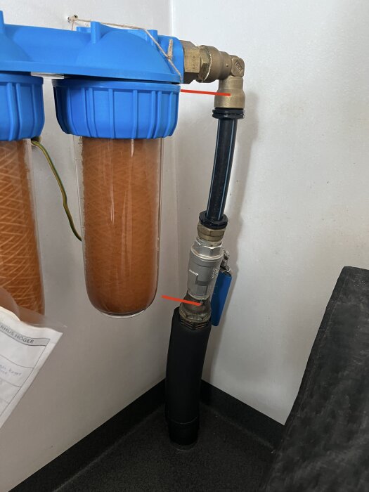 PEM-slang och vattenfilterhus i garaget, med kopplingar som inte är fästa mot väggen; röda streck markerar förslag på fästpunkter.