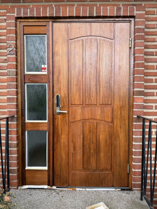 Renoverad ytterdörr med ny behandling av benarolja, omgiven av tegelvägg och glasruta, efter uppdatering.