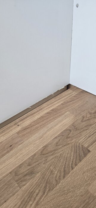 Ojämnt monterad bänkskiva mot väggen i ett kök med trägolv. Diskussion om att åtgärda snett hus och bästa sättet för kakeluppsättning.