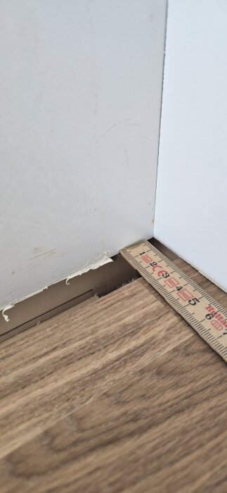 Måttstock visar mellanrum mellan skev vägg och ny bänkskiva i kök, bakgrund av träytor och väggen.