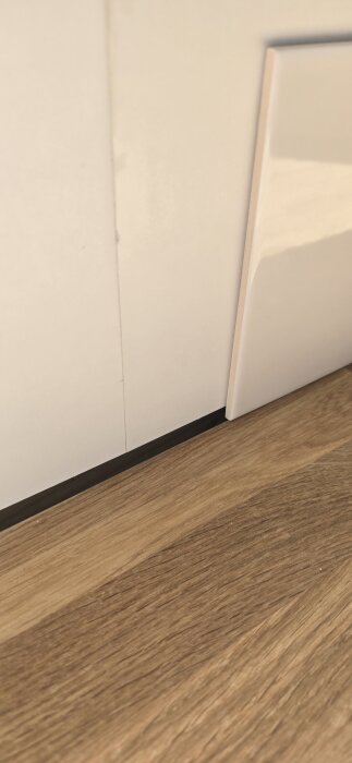 Ojämt mellanrum mellan bänkskiva och vägg visar en sned installation. En kakelplatta är lutad mot väggen ovanför trägolvet.