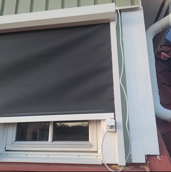 Vertikalmarkis installerad över ett fönster med en synlig anslutningskabel inkopplad i ett vägguttag bredvid.