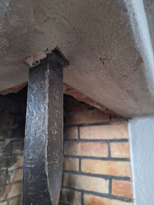 Grov vertikal järnpinne i murad öppna spis, fästad i ramen ovantill. Frågeställning om den är bärande hinder för spiskasettinstallation.