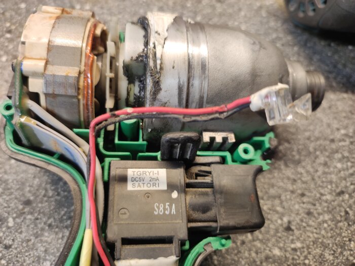 Öppen eldriven motor med exponerade kablar och komponenter, lagad med tejp och värmebehandlad dekal för reparation och fortsatt användning.