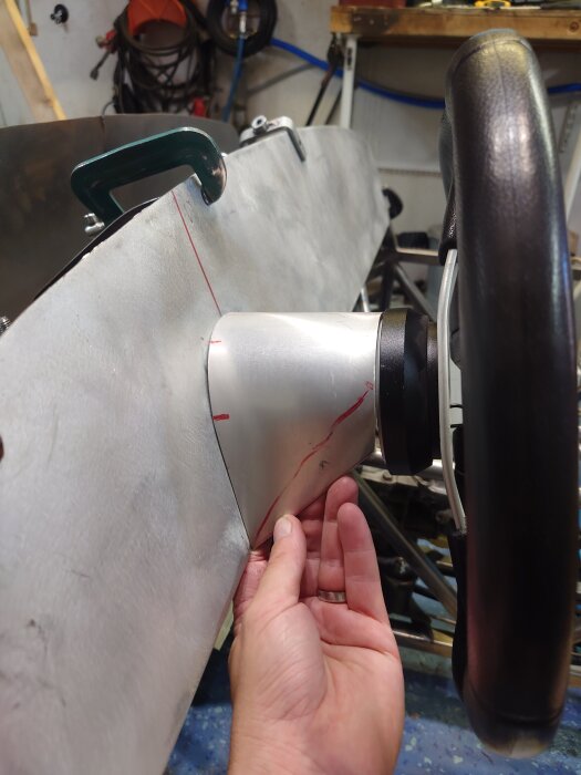 Hand håller en metallpanel med ett rattnav och monteringsverktyg i garageinställning.