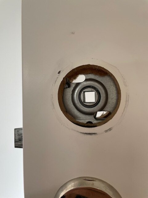 Närbild av innerdörr med avlägsnat dörrhandtag, synliga smutsspår och skador i färgen runt hålet där handtaget suttit monterat.