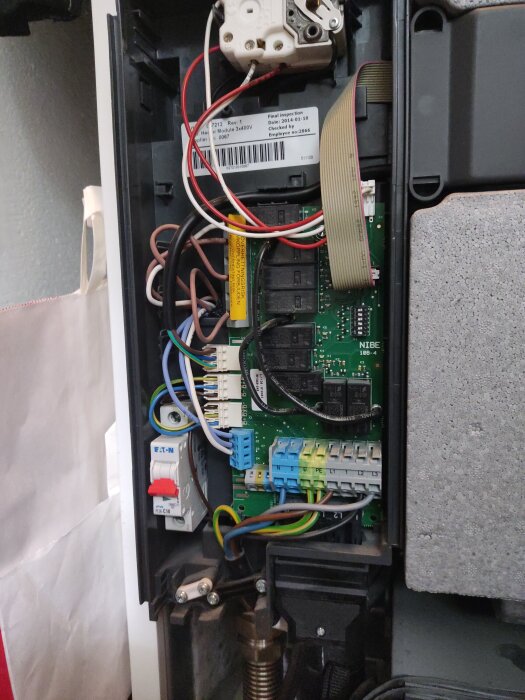 Elektrisk säkringsbox med kretskort, kablar och etiketter inuti en apparat. Säkringen märkt "Eaton" med röd avstängningsknapp.