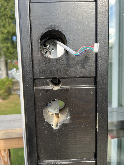 Närbild av en dörrkant med två borrade hål för låshusmontering, där låshuset inte är tillräckligt inskjutet för att möjliggöra låsinstallation.