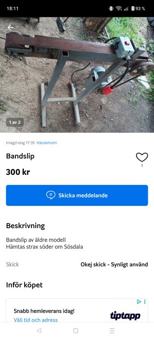 Äldre bandlip av metall med motor och strömbrytare, placerad på en utomhusyta med gräs och jord.