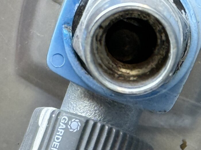 Närbild av en blå och metallisk vattenutkastare med en skadad eller lös komponent, märkt med "GARDENA".