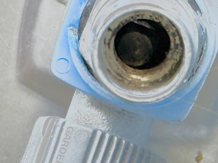 Närbild av en sexkantig vattenutkastare på en husvägg med inskjutet främmande föremål, mot bakgrund av en ljusare yta.