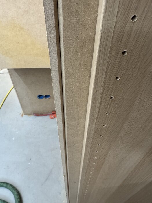MDF-paneler monterade på plywood med fasade hörn och hål för hyllplan. Del av byggprojekt med garderobsdörrar och bokhylla i ask.