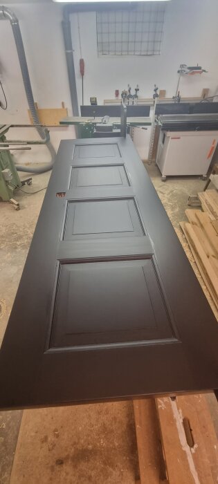 Svartmålad dörr med paneler ligger på arbetsbänk i verkstad, förvandlad till sänggavel enligt projektbeskrivning.